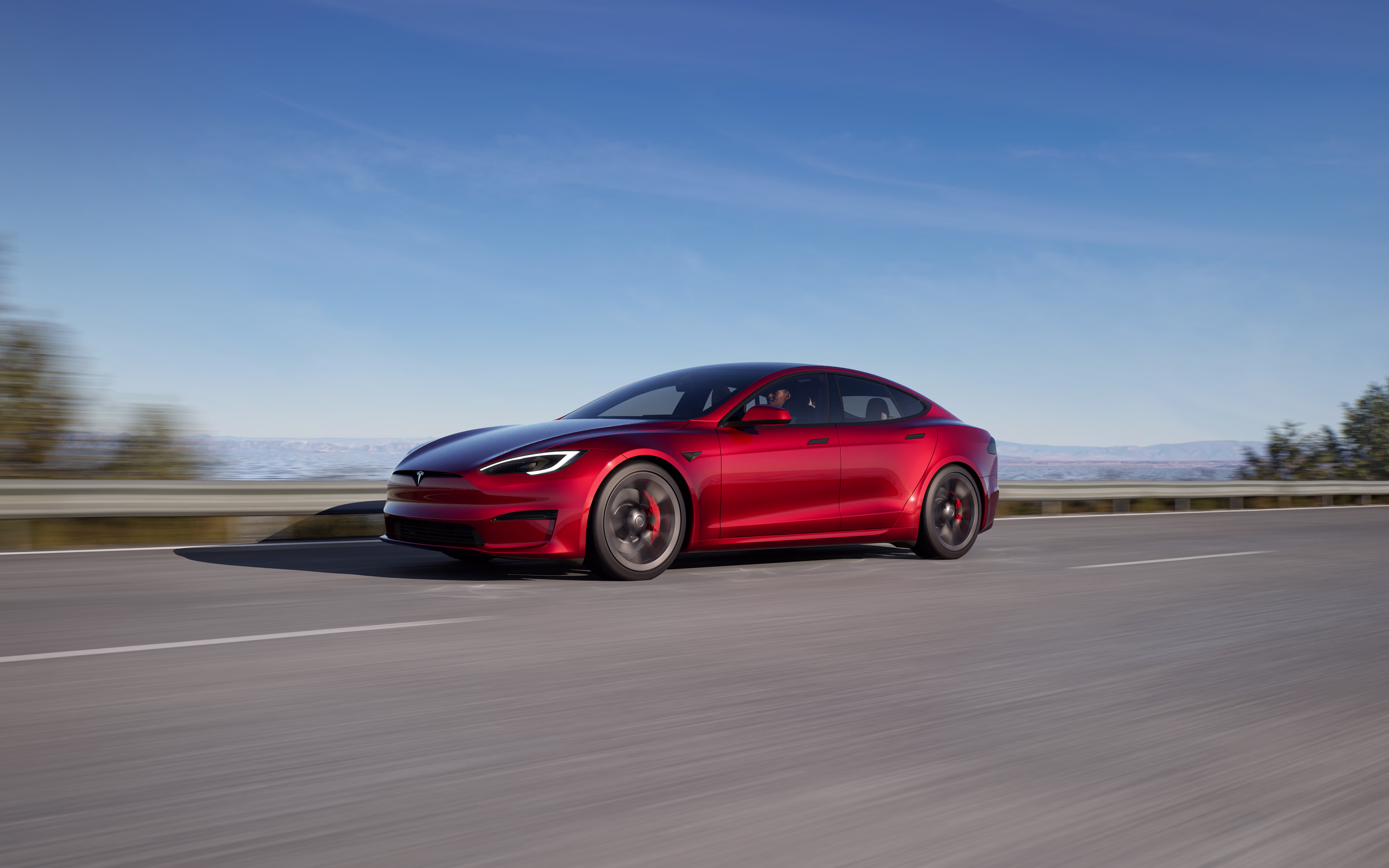 Red Model 3 driving down a lakeside road