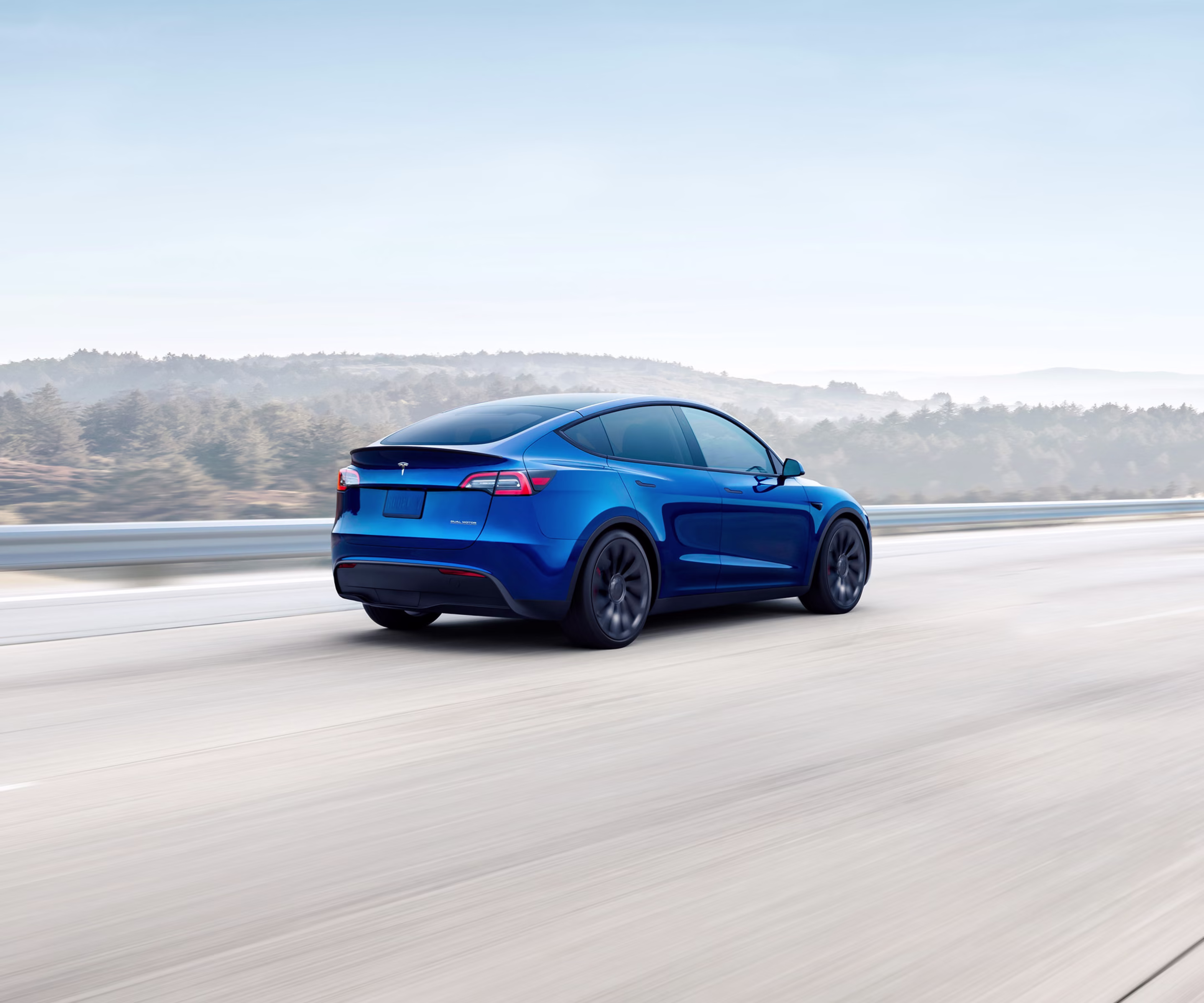 Red Model 3 driving down a lakeside road